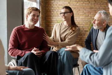 Psychotherapist comforting young man in wheelchair during group therapy session