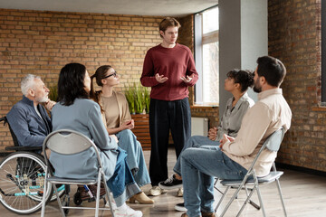 Young man leading group therapy session with diverse people listening attentively