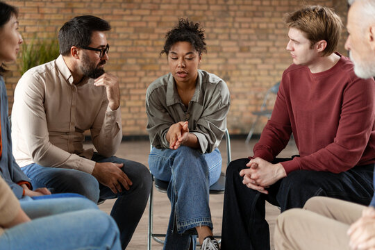 Diverse people sitting in circle supporting each other during group therapy session