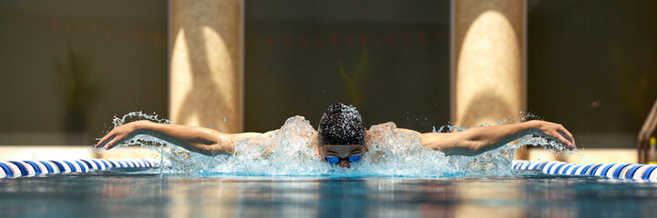 A swimmer executes a butterfly stroke in an indoor pool, exhibiting determination and focus. Concept of athletic perseverance and dedication in competitive sports.