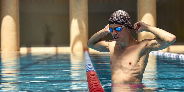 A young male swimmer adjusts his goggles at the poolside before starting his training session. Concept of preparation and focus in competitive swimming.