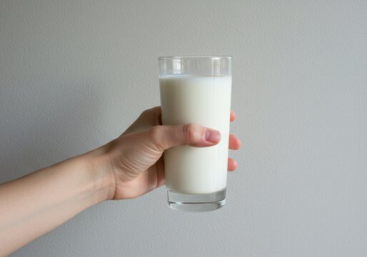 Hand holding a glass of fresh milk against a neutral background