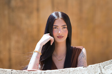 A young, beautiful brunette woman with long hair rests her cheek on her hand and looks thoughtful...