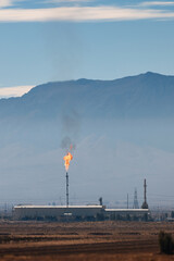 An industrial facility in Iran with a torch burning associated gases, Against the backdrop of mountains. Flares of Iranian oil refinery and smoking in the air, A factory hidden underground