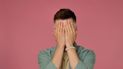 Man Hiding Face with Hands on Pink Background in Studio Setting