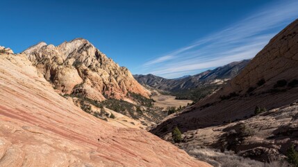 Fototapeta premium Stunning mountain landscape under clear blue sky with wispy clouds, textured warm-hued rock formations, smooth striations, and crevices in foreground.