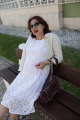 Elegant woman relaxing on bench in white dress and sunglasses
