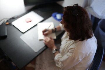 Woman writing notes at home office desk working remotely