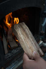 Close-up of firewood burning inside a black metal stove, with bright orange flames and glowing...