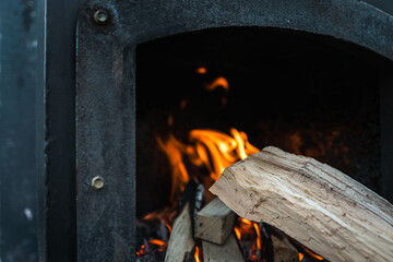 Close-up of firewood burning inside a black metal stove, with bright orange flames and glowing...