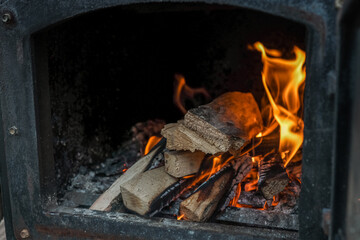 Close-up of burning firewood inside a black metal stove, with glowing embers and orange flames...