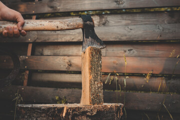 Close-up of a hand holding an axe embedded in a vertical log, ready for splitting firewood outdoors...