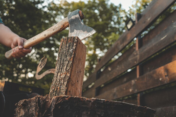 Close-up of a hand holding an axe embedded in a vertical log, ready for splitting firewood outdoors...
