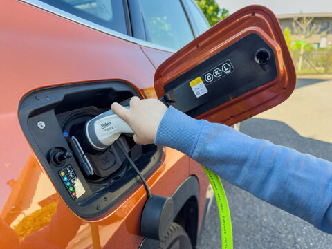 Paris, France - Apr 30, 2025: Child's hand connects Valeo Ineez charger to orange electric vehicle on a sunny day, showing the EV socket, cable and charging port lid