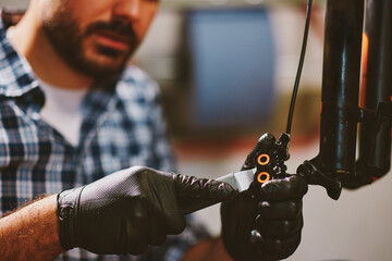 Bicycle mechanic repairing brakes in workshop: focus on hands and tools