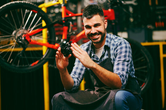Smiling bicycle mechanic holding bike part in workshop