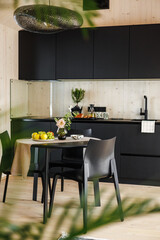 Bright Scandinavian-style kitchen with black cabinetry, a cozy dining table featuring fresh fruit, floral centerpiece, and dotted ceramics in a minimal modern interior