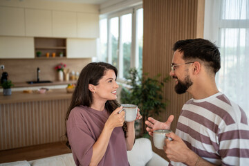 Happy couple enjoying morning coffee, talking and smiling in modern kitchen