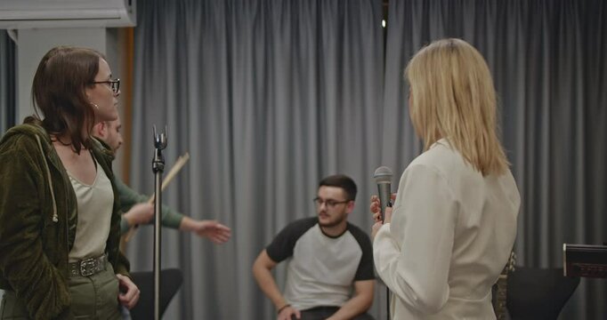 Music band practicing in a studio before their concert. The lead singer rehearses with the band, receiving feedback from the manager or producer.