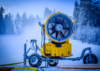 Snowmaking machine operates on a winter day in a ski resort, creating artificial snow for skiing...
