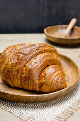 A baked golden brown croissant resting on a round wooden plate styled with a rustic theme,...