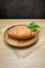 A golden brown croissant placed on a rustic wooden plate, with green leaves for decoration with a...