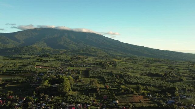 Mount Apo slopes dominate a wide Mindanao valley with farm plots village homes and low clouds lit by soft morning sunlight near Davao