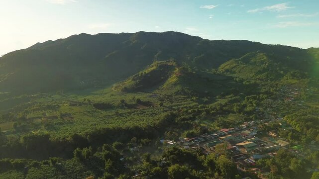 Early morning aerial view highlights rolling green hills, scattered farms, and peaceful village life beneath Mount Apo, surrounded by lush tropical vegetation in Davao, Mindanao.