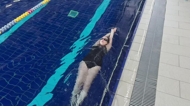 Professional female swimmer. Woman athlete swimmer training at swimming pool. Woman swimmer performing swimming in backstroke or back crawl style technique. Endurance sport professional swimming