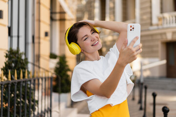stylish woman wearing yellow headphones listening to music taking pictures on smartphone camera