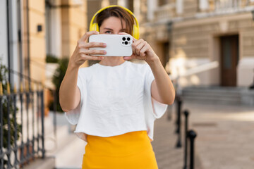 stylish woman wearing yellow headphones listening to music taking pictures on smartphone camera