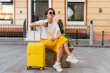 stylish woman traveling with yellow suitcase in Europe