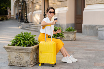 stylish woman traveling with yellow suitcase in Europe
