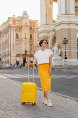 stylish woman traveling with yellow suitcase in Europe