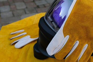 Welding gloves on top of the welding helmet. Yellow apron backdrop. Protective clothing for...