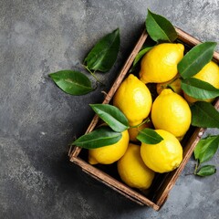 Fresh, juicy lemons and vibrant green leaves, perfectly arranged in a rustic wooden crate. The bright colors pop against a textured, dark gray surface. 