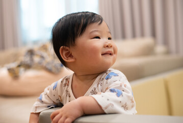 A little asian child baby proud for climb and hold onto playpen wall with his smile. He practice to standing and walking. Development Baby aged of 8 months concept.