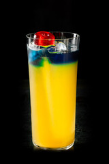 Refreshing layered cocktail in a tall glass with blue and yellow hues, topped with ice cubes and a red cherry, perfect for summer themes, parties, or drink menus.