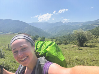 Hiking tourism adventure. Backpacker hiker woman taking selfie picture. Hiker girl lady tourist with backpack walking near mountain. Young happy woman enjoy hike trekking tourism active vacation