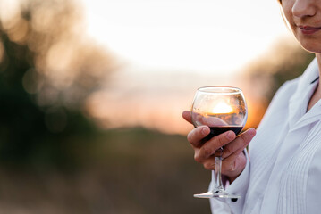 Smiling girl with a glass of wine on vacation. Silhouette of the setting sun in the glass. Soft sunlight. 