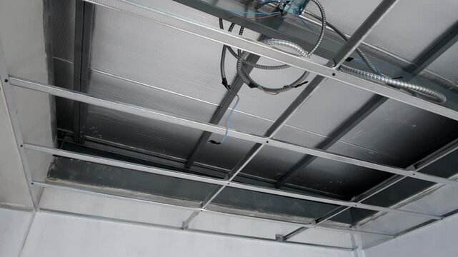 House interior renovation in progress, detailing complex construction of metal framework for suspended ceiling installation and intricate electrical wiring system.