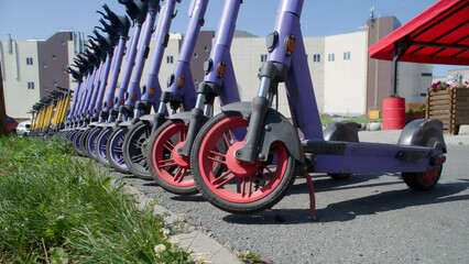 A line of purple and yellow electric scooters parked on a city sidewalk, highlighting modern micro-mobility services in an urban environment. Photo. Selective focusing