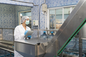 Drinking water production plant. 20 Liter bottled water filling machine plant. Worker produces inspecting quality of 20 Liter bottled water on conveyor belt during filling in drinking water factory