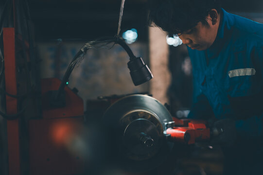 A worker in a blue uniform operates a lathe machine in a dimly lit workshop, focusing intently on the metalworking process. - Powered by Adobe