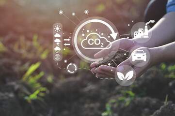 Hands holding soil with digital icons representing CO2 emissions, sustainability, and environmental...