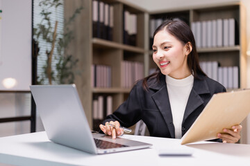 Young businesswoman smiling and working using laptop and holding folder with documents sitting at...
