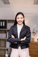 Young Asian manager smiling with arms crossed, showing confidence and professionalism in a modern...
