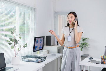 Businesswoman is standing in a bright, modern office, talking on her phone and gesturing with her hand, suggesting she's engaged in a discussion or giving instructions