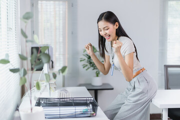 Young Asian businesswoman celebrating success in a modern office, radiating joy and excitement over a recent achievement while working at her desk with a laptop