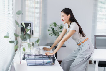 Smiling and working at her computer in a modern office, a young businesswoman enjoys a productive workday, embracing the efficiency and creativity of her corporate environment